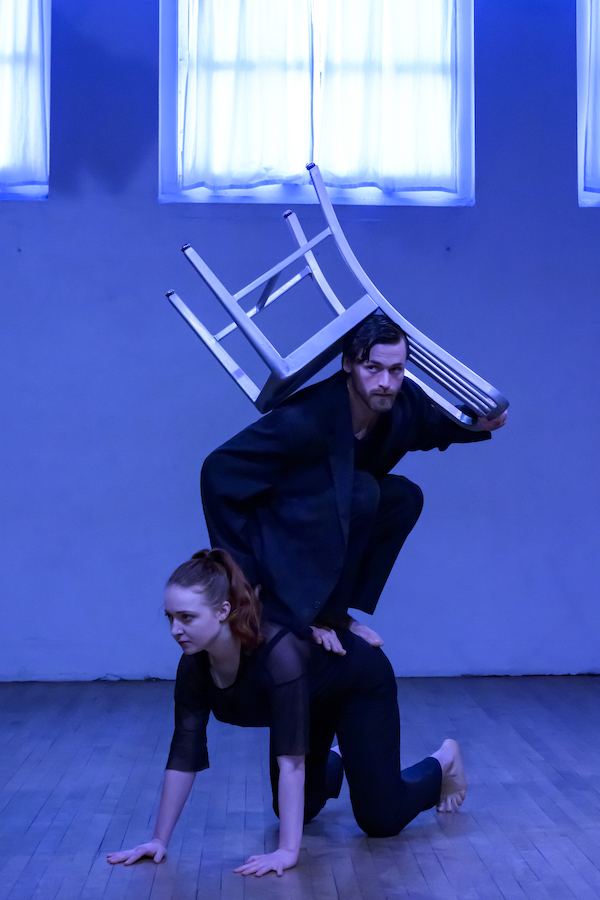 One dancer sits atop another with a chair on his head. 
